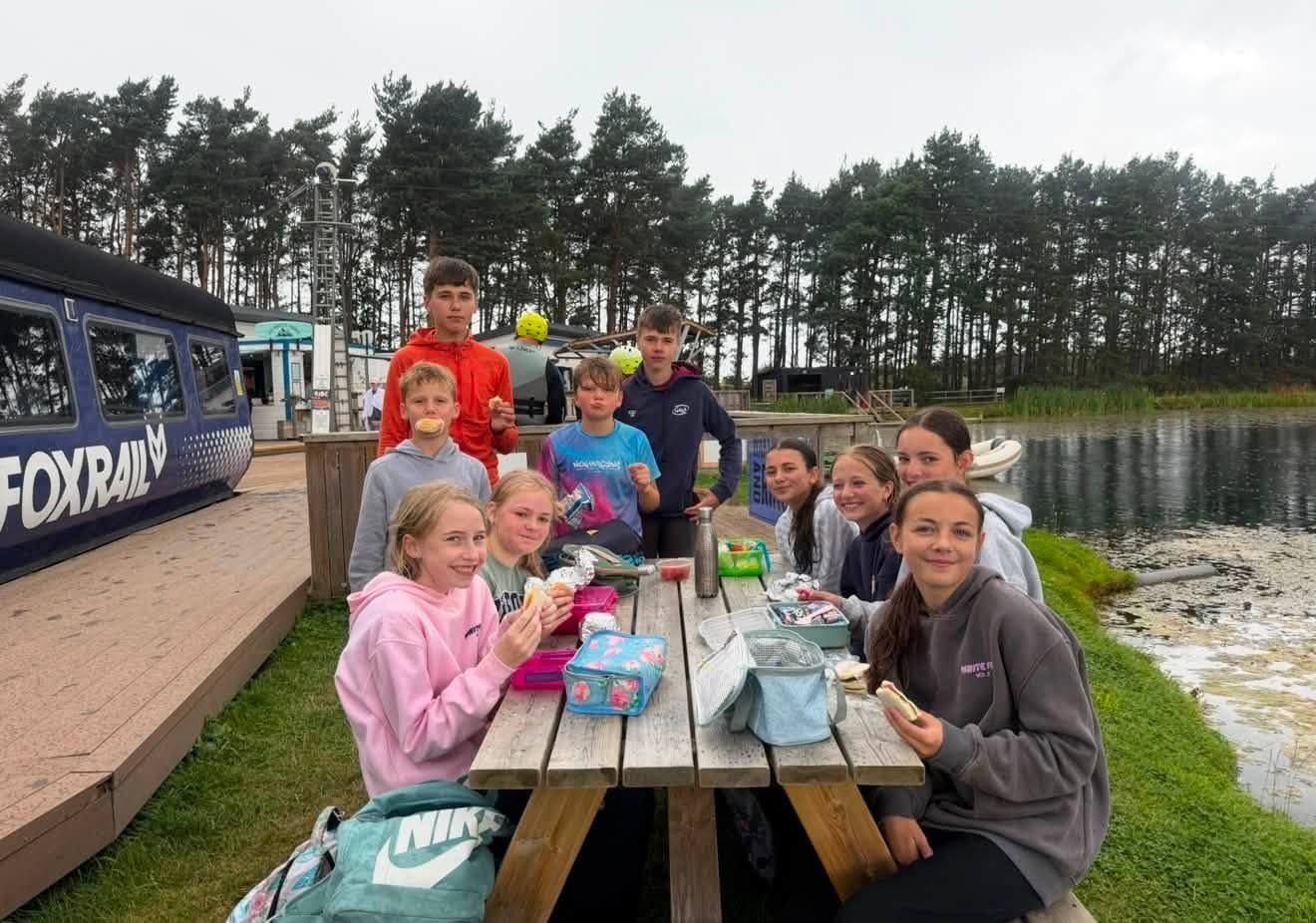 Young people sharing lunch at a picnic table beside the water